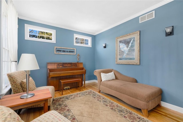 living area with visible vents, baseboards, wood finished floors, and ornamental molding