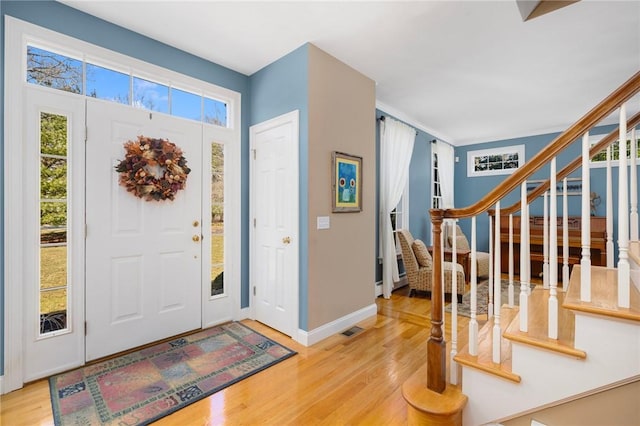 foyer entrance with stairway, baseboards, visible vents, and wood finished floors