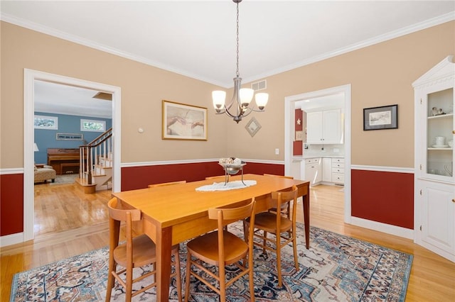 dining space with visible vents, ornamental molding, light wood finished floors, a chandelier, and stairs