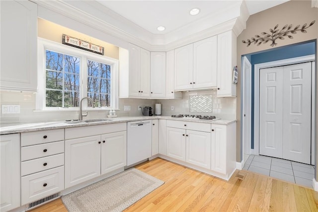 kitchen featuring visible vents, light wood-style flooring, a sink, white cabinetry, and white appliances