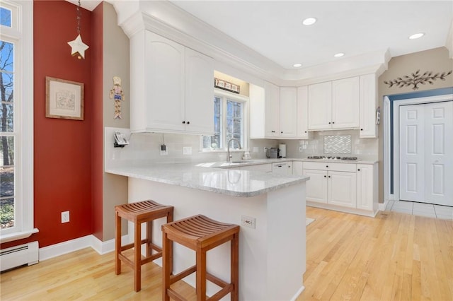 kitchen featuring white cabinetry, a peninsula, a breakfast bar, and a baseboard heating unit