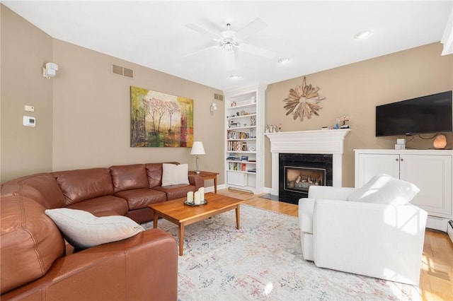 living area with visible vents, built in shelves, a ceiling fan, and light wood finished floors