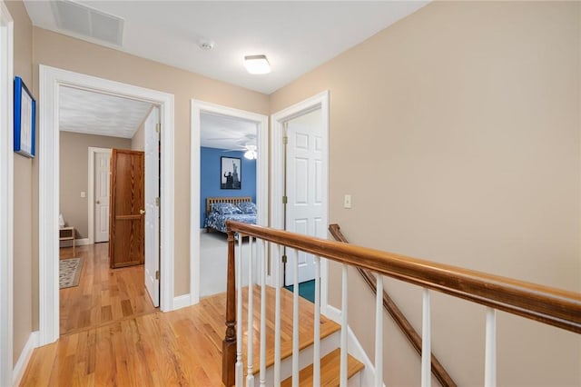 corridor featuring an upstairs landing, light wood-style floors, visible vents, and baseboards