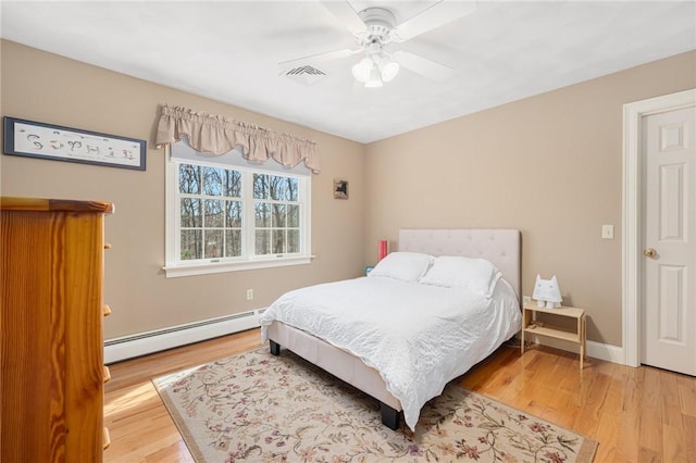 bedroom featuring visible vents, a baseboard heating unit, baseboards, and wood finished floors