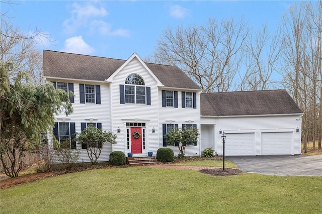 colonial-style house with aphalt driveway, a front yard, a garage, and roof with shingles