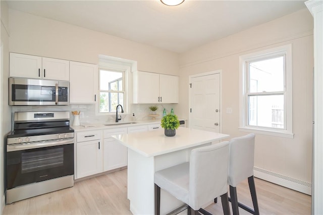 kitchen with a sink, white cabinetry, stainless steel appliances, light countertops, and baseboard heating