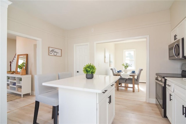 kitchen featuring a breakfast bar, stainless steel appliances, light countertops, light wood-style floors, and a center island