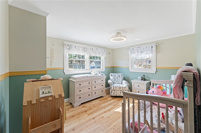 bedroom featuring crown molding, a nursery area, and light wood finished floors