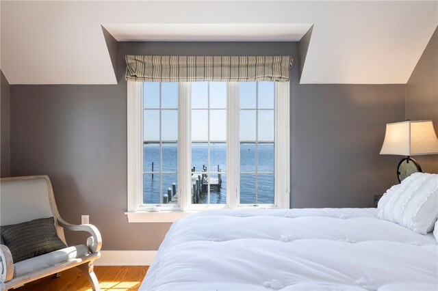 bedroom with lofted ceiling, wood finished floors, a water view, and baseboards