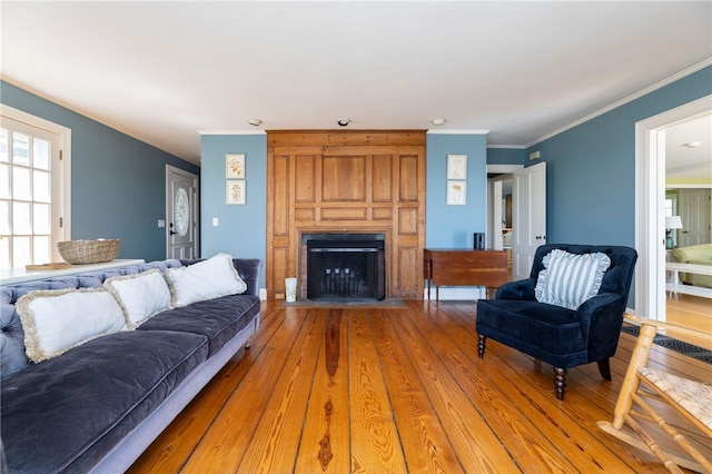 living room with a fireplace with flush hearth, crown molding, and light wood finished floors