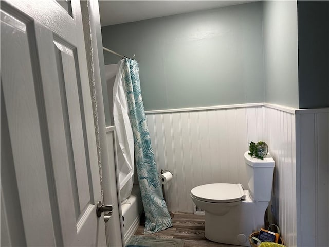 full bath featuring a wainscoted wall, toilet, shower / bath combo with shower curtain, and wood finished floors