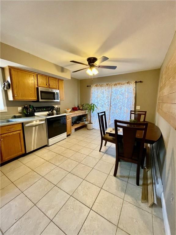 kitchen with appliances with stainless steel finishes, light tile patterned flooring, brown cabinetry, light countertops, and ceiling fan