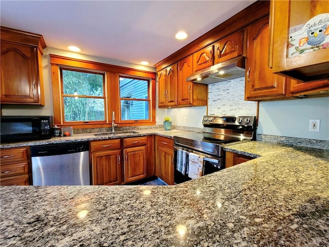 kitchen featuring a sink, dark stone countertops, under cabinet range hood, and stainless steel appliances