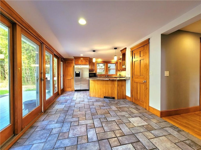 kitchen featuring a healthy amount of sunlight, baseboards, a peninsula, stainless steel refrigerator with ice dispenser, and brown cabinetry