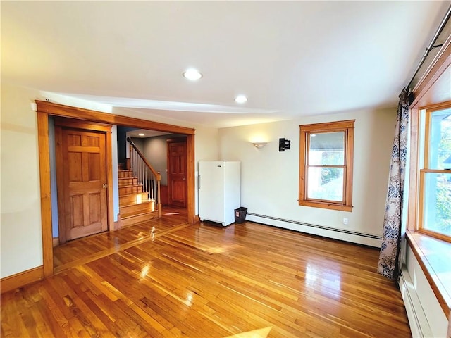 empty room with a baseboard heating unit, stairs, light wood-type flooring, baseboard heating, and recessed lighting