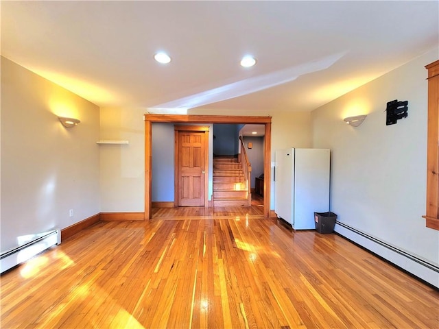 spare room featuring light wood finished floors, baseboard heating, stairs, and baseboards