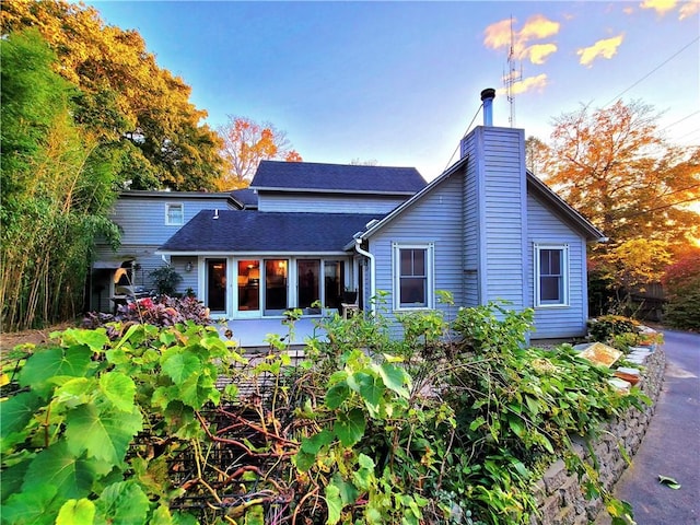 rear view of property with a shingled roof and a chimney