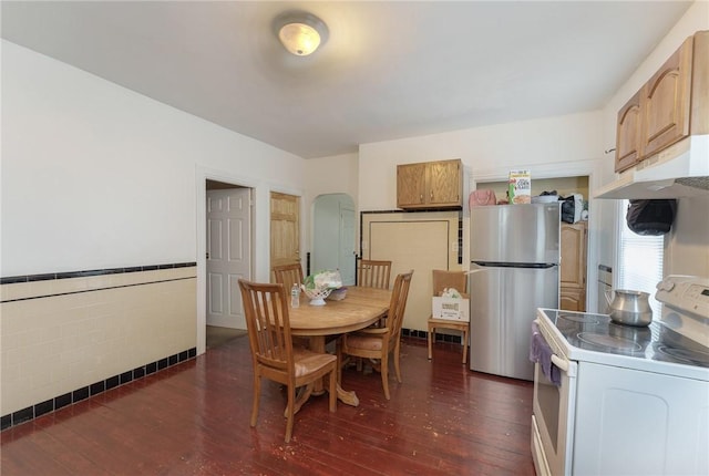 dining room featuring arched walkways, dark wood-style floors, tile walls, and a wainscoted wall