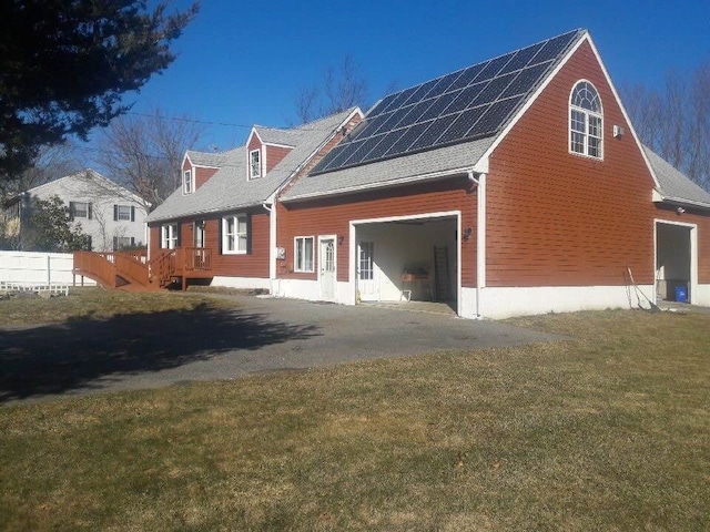 view of home's exterior with solar panels, aphalt driveway, roof with shingles, a garage, and a yard