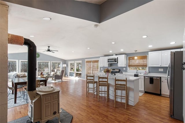 kitchen with a ceiling fan, appliances with stainless steel finishes, a wood stove, and light wood finished floors