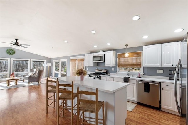 kitchen featuring a breakfast bar area, appliances with stainless steel finishes, light wood-style floors, white cabinetry, and a ceiling fan