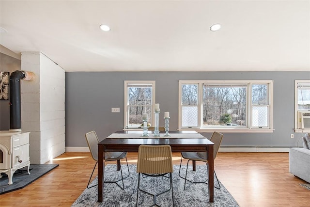 dining room with a wealth of natural light, a baseboard radiator, light wood-style flooring, and a wood stove