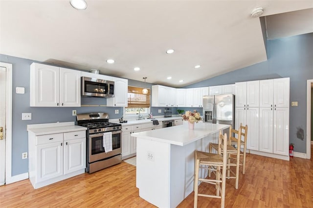 kitchen with a breakfast bar, vaulted ceiling, white cabinets, appliances with stainless steel finishes, and a center island