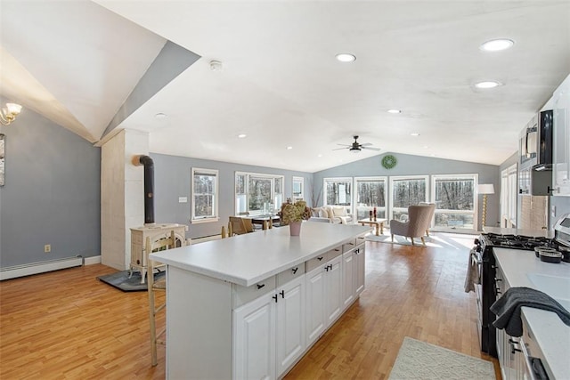 kitchen featuring lofted ceiling, a wood stove, ceiling fan, light wood-style floors, and gas range