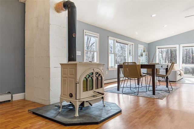 dining room with a baseboard radiator, lofted ceiling, a wood stove, recessed lighting, and light wood-type flooring