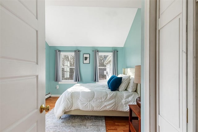 bedroom with lofted ceiling, wood finished floors, baseboards, and baseboard heating