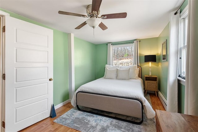 bedroom featuring light wood-type flooring, a baseboard radiator, baseboards, and ceiling fan