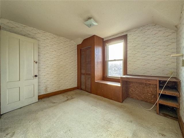 additional living space featuring a textured ceiling, vaulted ceiling, carpet flooring, and wallpapered walls