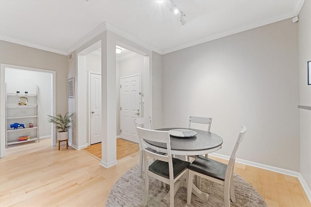 dining room featuring crown molding, rail lighting, light wood-style floors, and baseboards