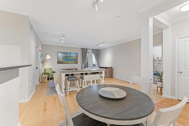 dining area featuring light wood finished floors, rail lighting, crown molding, and baseboards