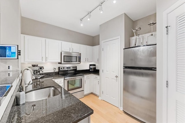 kitchen with light wood-type flooring, dark stone countertops, appliances with stainless steel finishes, white cabinetry, and a sink