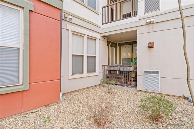 entrance to property featuring visible vents, a balcony, and stucco siding