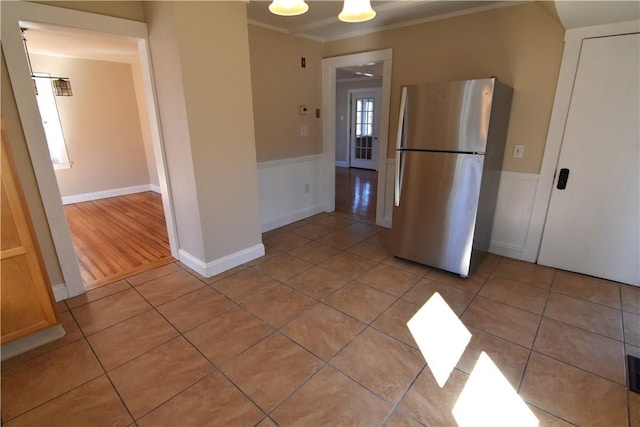 kitchen with light tile patterned floors, a wainscoted wall, crown molding, and freestanding refrigerator