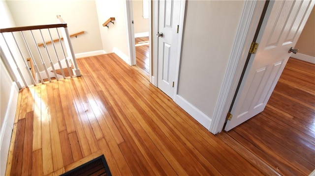 hallway featuring light wood-type flooring, an upstairs landing, and baseboards