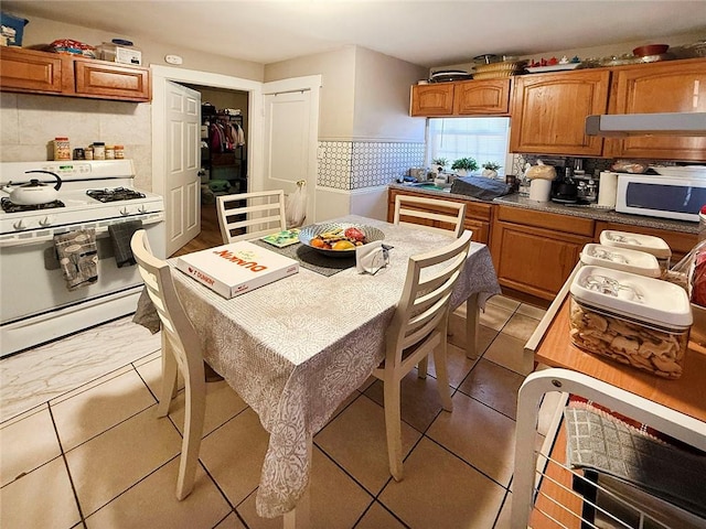 kitchen featuring under cabinet range hood, white appliances, brown cabinets, and tile patterned flooring