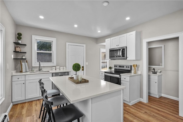 kitchen featuring a sink, open shelves, a kitchen breakfast bar, stainless steel appliances, and white cabinets