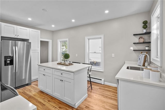 kitchen with open shelves, a baseboard heating unit, stainless steel fridge with ice dispenser, light wood-style floors, and a sink