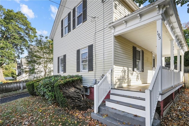 view of side of home featuring covered porch and fence