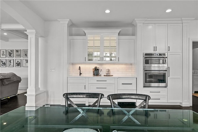 50 Kenyon Ave, East Greenwich, RI 02818 - kitchen featuring decorative columns, decorative backsplash, white cabinetry, and stainless steel double oven