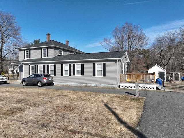 view of side of property featuring a wooden deck, roof with shingles, and a chimney