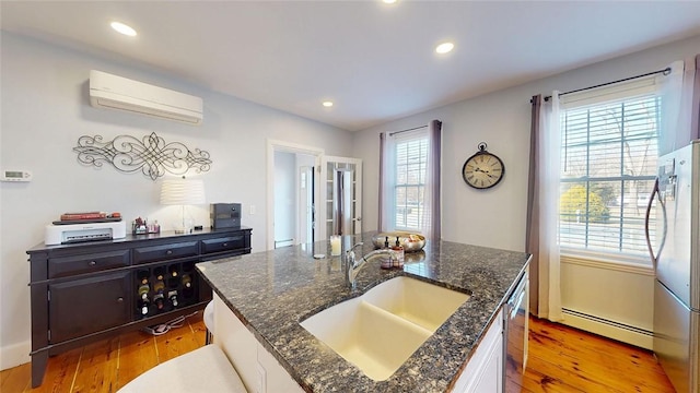 kitchen with a sink, a wall unit AC, freestanding refrigerator, light wood finished floors, and baseboard heating