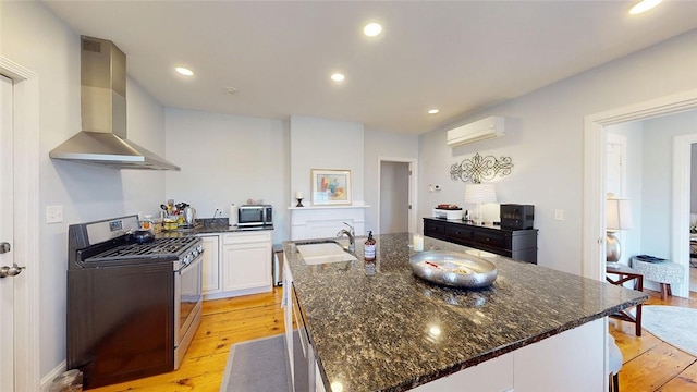 kitchen featuring a wall unit AC, appliances with stainless steel finishes, white cabinets, wall chimney exhaust hood, and a sink