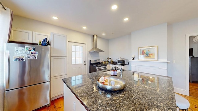 kitchen featuring recessed lighting, a kitchen island with sink, stainless steel appliances, light wood-style floors, and wall chimney exhaust hood