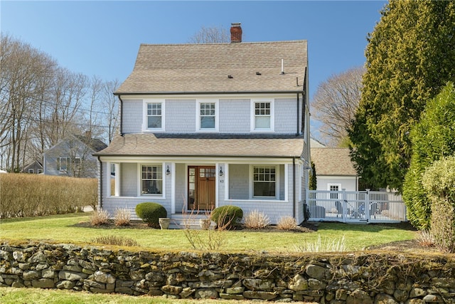 view of front facade featuring fence, roof with shingles, covered porch, a chimney, and a front lawn