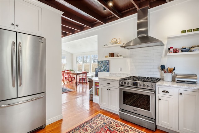 kitchen with wall chimney range hood, beam ceiling, light wood-style floors, stainless steel appliances, and open shelves