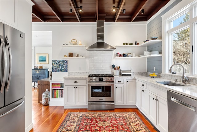 kitchen with open shelves, light wood-style flooring, appliances with stainless steel finishes, wall chimney exhaust hood, and a sink